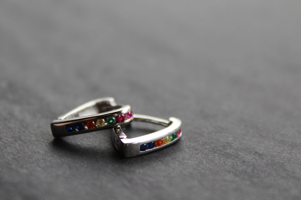 Pair of silver hoop earrings with colorful gemstones on a dark surface