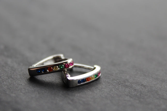 Pair of silver hoop earrings with colorful gemstones on a dark surface