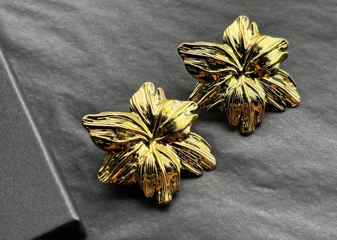 Pair of gold floral earrings on a dark gray background