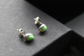 Pair of green stud earrings on a dark surface