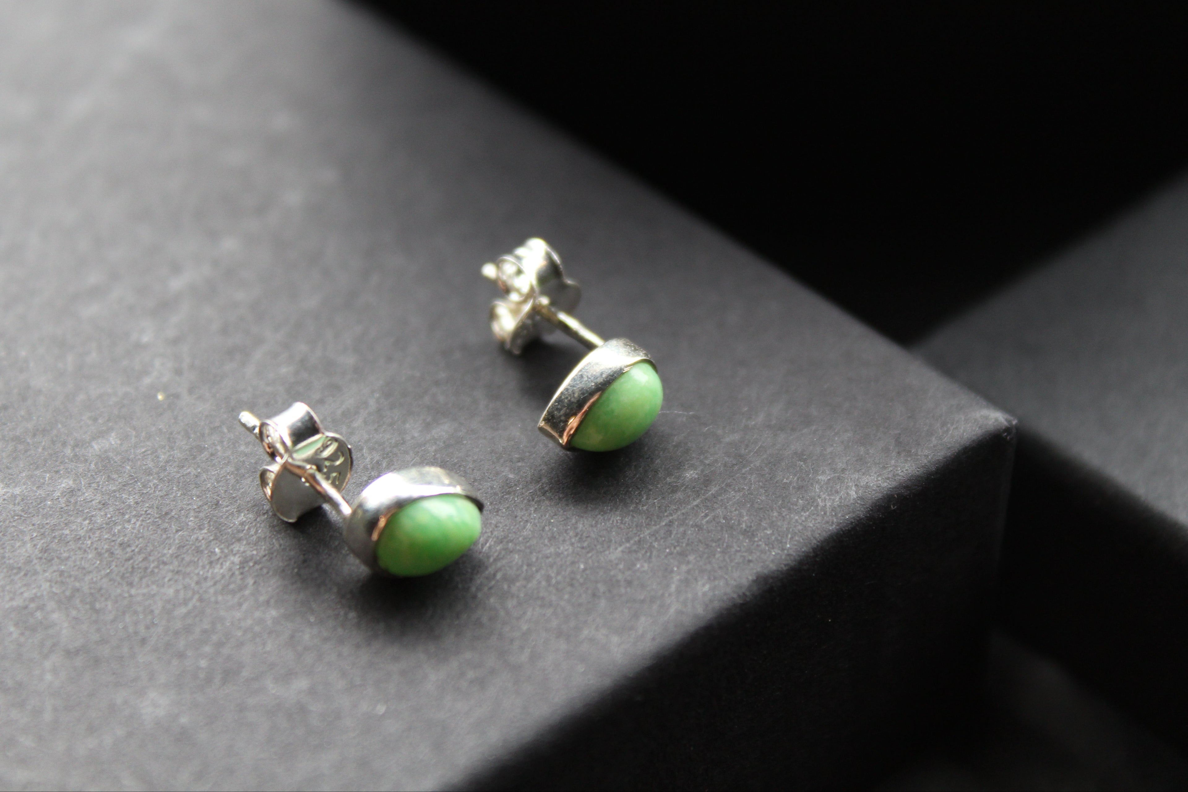 Pair of green stud earrings on a dark surface