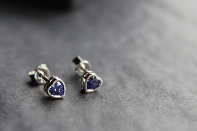 Pair of silver heart-shaped earrings with blue stones on a gray surface